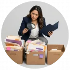 A woman searching for evidence of compliance and controls in several disheveled boxes of documents.